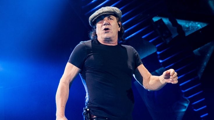 Brian Johnson of AC/DC performing on stage during a high-energy classic rock concert, wearing his signature flat cap.