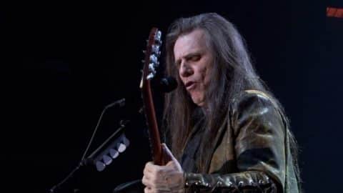 Frank Marino performing live on stage, playing an electric guitar and singing into a microphone.