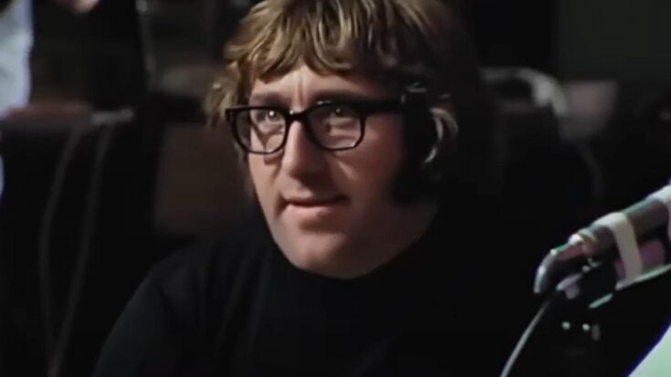 Mal Evans seated in a recording studio during the Beatles’ “Get Back” sessions, wearing dark glasses and a black turtleneck.