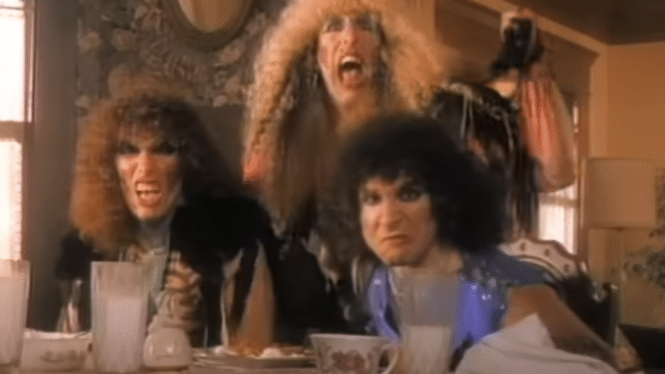 Members of Twisted Sister dressed in flamboyant costumes shouting at a breakfast table in a scene from the