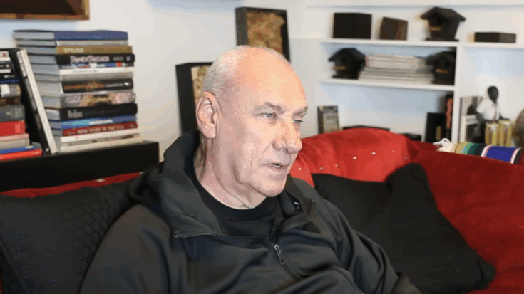 Bill Ward sitting on a couch during an interview, surrounded by books and memorabilia, reflecting on the legacy of Black Sabbath.