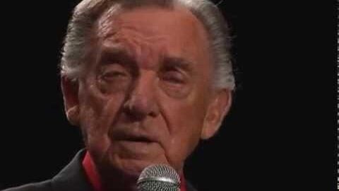 Ray Price performing live on stage, holding a microphone in a close-up shot.
