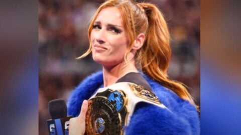 WWE star Becky Lynch holding a championship belt and smirking during a live event.