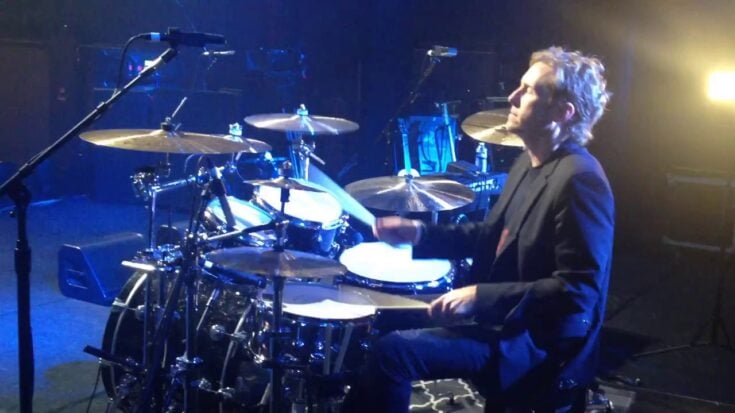Josh Freese performing on drums during a live concert, captured under stage lights.
