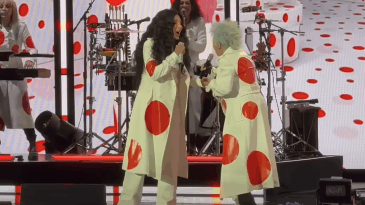 Cher and Cyndi Lauper perform together on stage at the Hollywood Bowl during Lauperโs farewell concert, both wearing matching white coats with red polka dots.