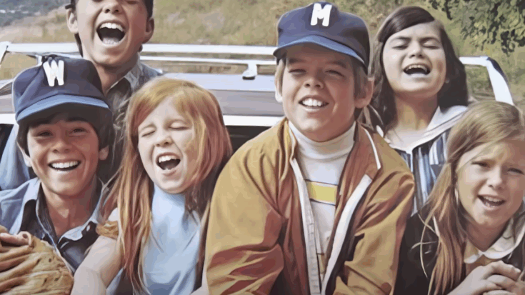 Group of smiling kids in the 1970s riding in the back of a station wagon, enjoying a carefree day together.
