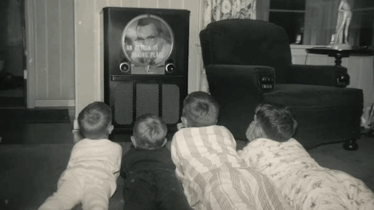 Four children in pajamas lying on the floor watching a black-and-white television in the 1970s living room.