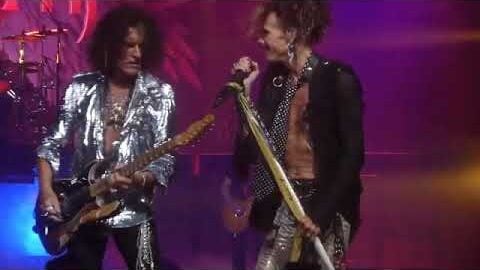 Steven Tyler and Joe Perry performing together onstage, delivering a powerful rock performance under vibrant stage lights.