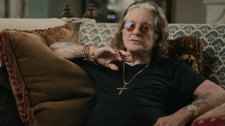 Ozzy Osbourne sitting on a sofa wearing sunglasses and a cross necklace during the BBC documentary Coming Home.