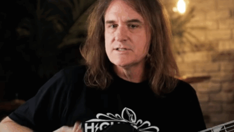 David Ellefson playing bass guitar in a studio setting with warm lighting and instruments in the background.