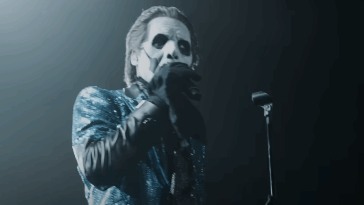 Tobias Forge of Ghost performing on stage under moody blue lighting, wearing his signature costume and theatrical makeup.