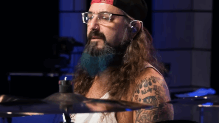 Mike Portnoy performing on drums during a studio session, wearing a cap and glasses.