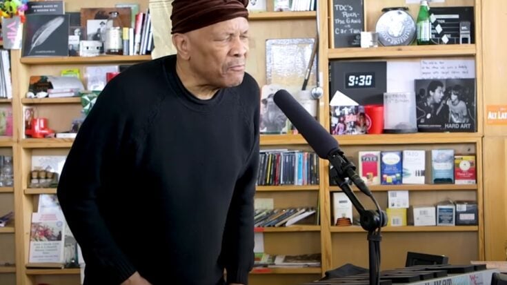 Roy Ayers performing at his NPR Tiny Desk Concert, standing behind a keyboard with a microphone in front of him.