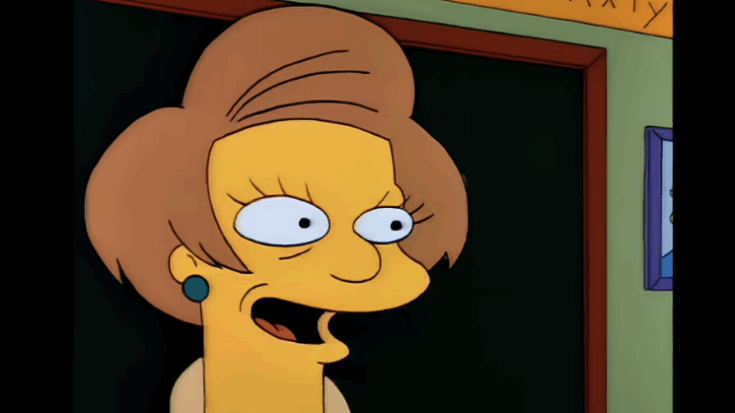 Edna Krabappel smiling in a classroom scene from The Simpsons.