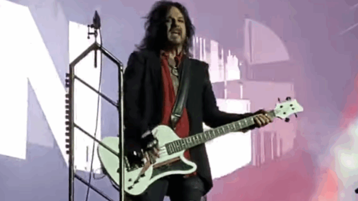 Nikki Sixx performing live with his white bass guitar during Mötley Crüe’s 2022 Toronto tour stop, captured onstage against a bright, colorful backdrop.
