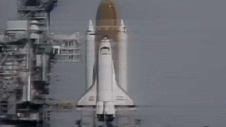 Space Shuttle Challenger on the launch pad moments before liftoff in 1986, with the orbiter and external fuel tank visible against the launch tower.