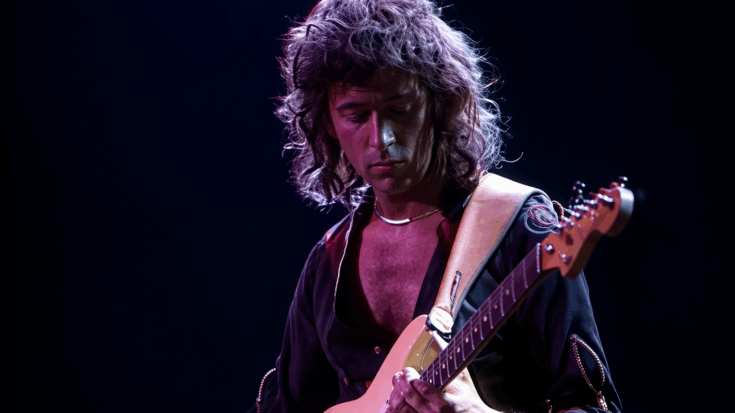 Ritchie Blackmore focuses on his guitar as he performs under moody purple stage lights.